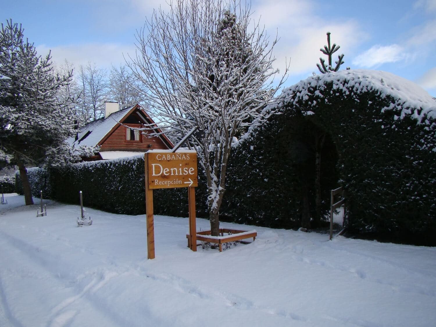 Entrada desde la vereda de las Cabañas Denise, con un cartel de ingreso y nieve