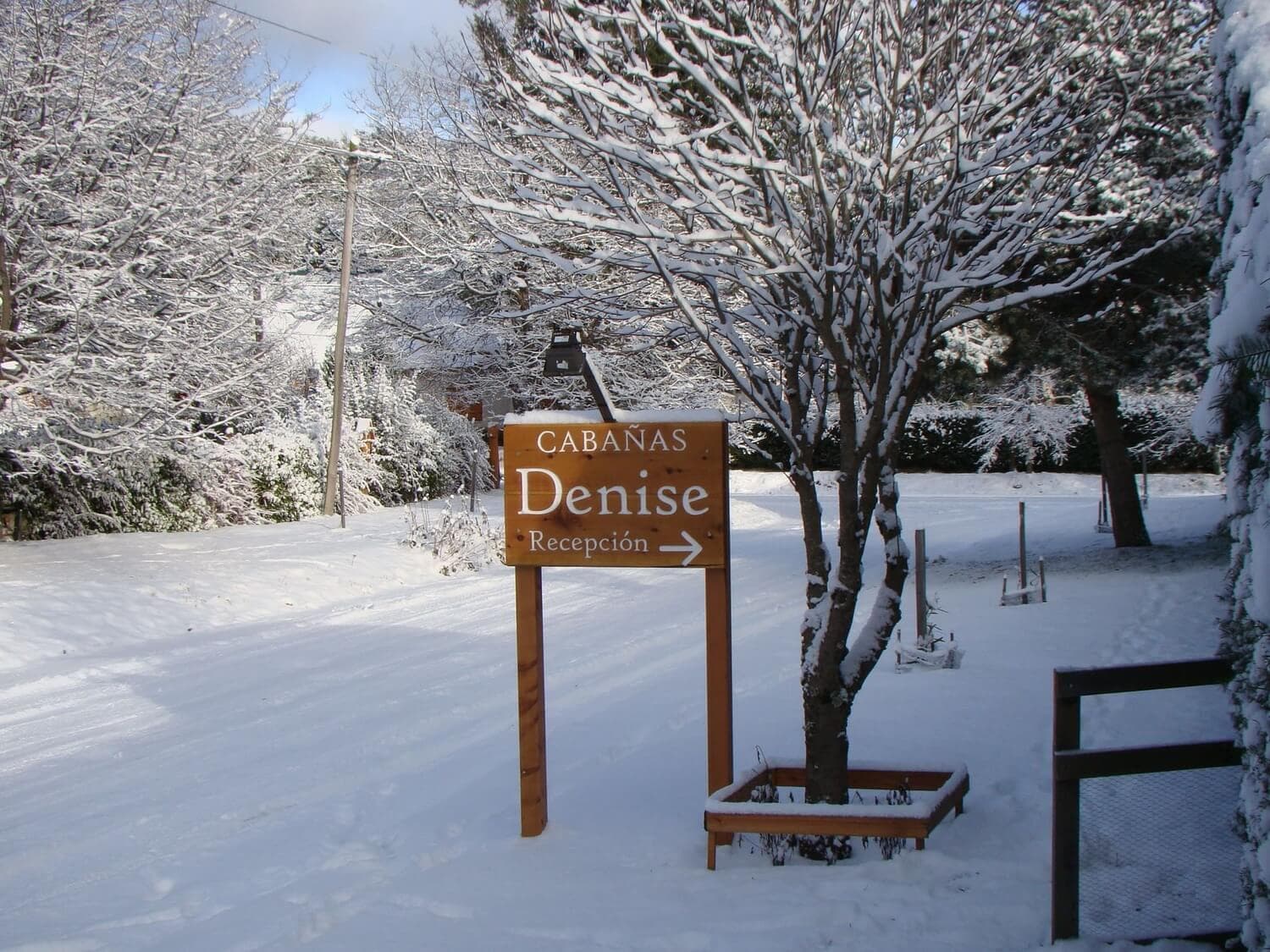 Cartel de ingreso a las Cabañas Denise, con la calle de fondo cubierta de nieve