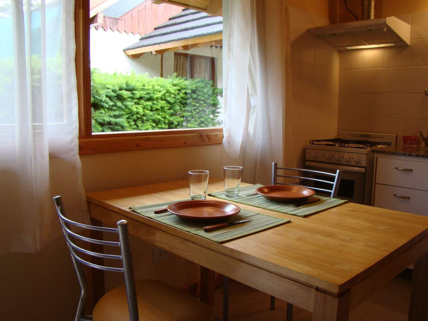 Mesa con platos, vasos y cubiertos, con vista de la ventana del monoambiente de Cabañas Denise